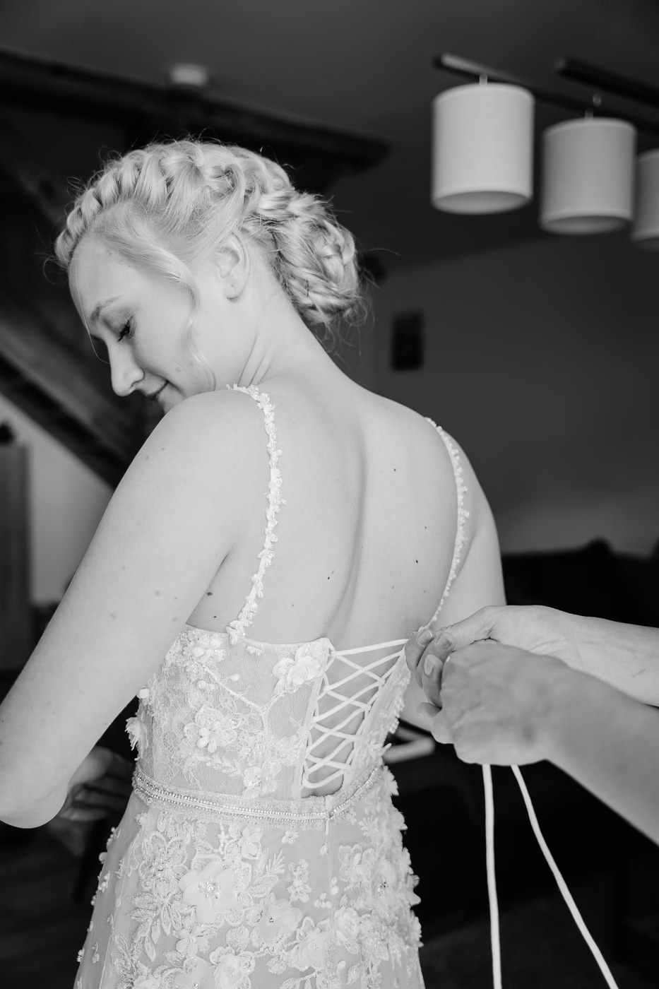 Getting Ready Hochzeit – Korsett des Brautkleides wird sorgfältig geschnürt, Braut lächelt, geflochtene Hochzeitsfrisur von hinten, Hochzeitsreportage Helmstedt Kathrin Skorpel