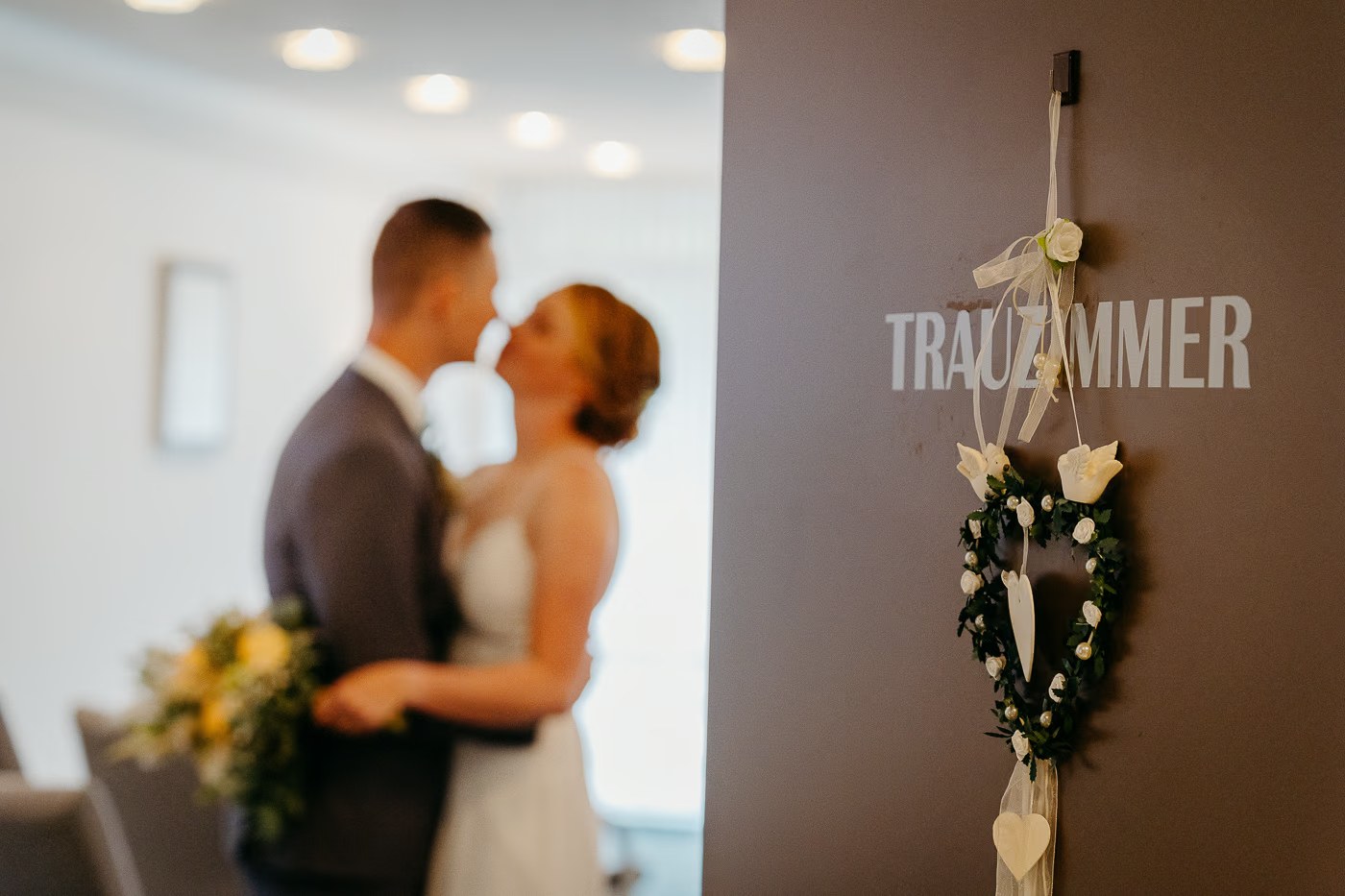Hochzeitsreportage Standesamt – Brautpaar küsst sich vor dem Schild Trauzimmer, authentische Hochzeitsfotos