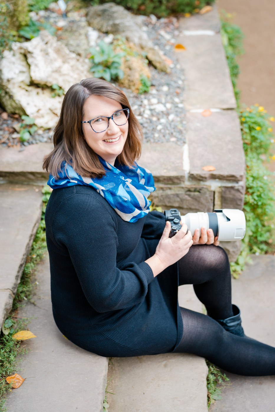 Portrait Kathrin Skorpel Peine – Fotografin sitzt l&auml;chelnd auf Steinstufen mit Kamera in der Hand, nat&uuml;rliches Herbstlicht, Hochzeitsfotografin Peine Kathrin Skorpel