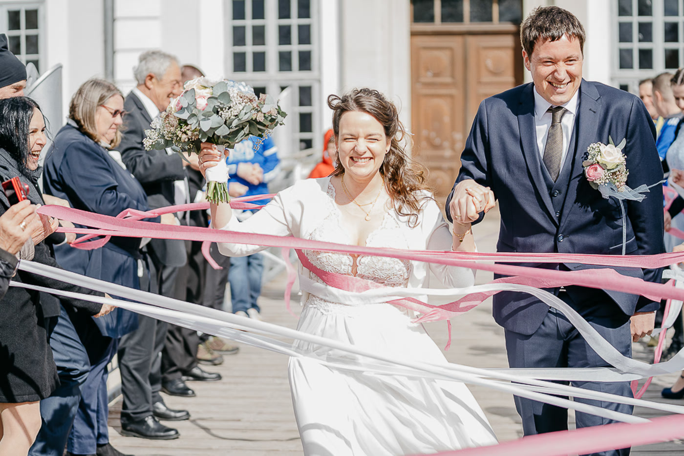 Standesamt Hochzeit Braunschweig – Brautpaar läuft strahlend lachend durch flatternde Bänder der jubelnden Gäste nach der standesamtlichen Trauung, pure Freude und Energie, Hochzeitsreportage Braunschweig Kathrin Skorpel