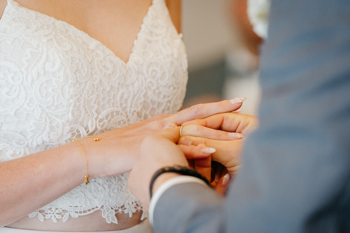 Standesamt Hochzeit Helmstedt – Nahaufnahme Ringtausch, Bräutigam steckt Braut den Ehering an den Finger, Spitzenkleid und goldenes Armband, zarter Moment, Hochzeitsfotografie Helmstedt Kathrin Skorpel